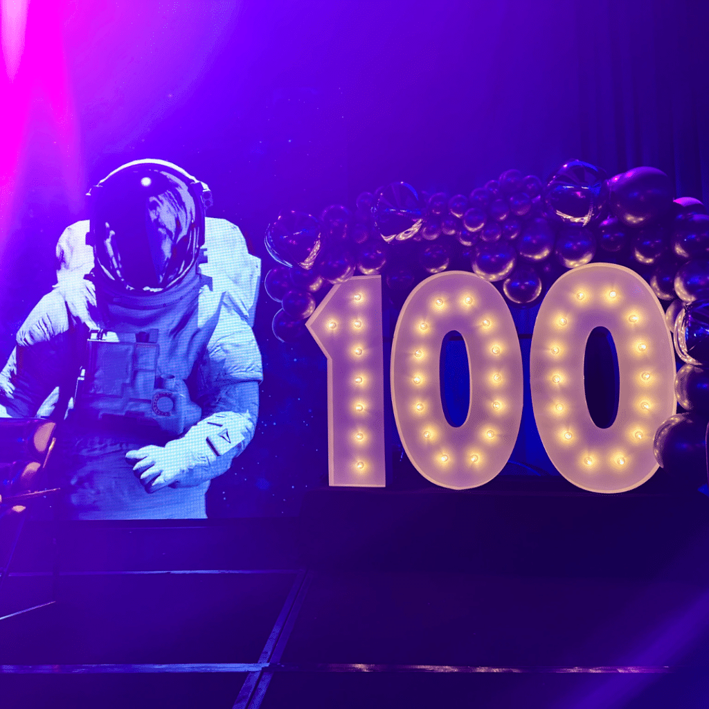 Marquee Number 100 beneath a balloon display beside an astronaut