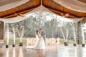 A bride and groom in an outdoor pavilion, posing in front of marquee letters that read 'Mr & Mrs'