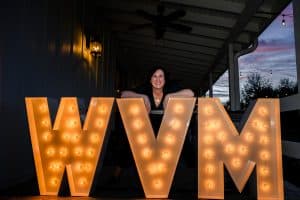 Woman leaning on her corporate marquee letters that say ‘WVM’ for Wedding Venue Map 