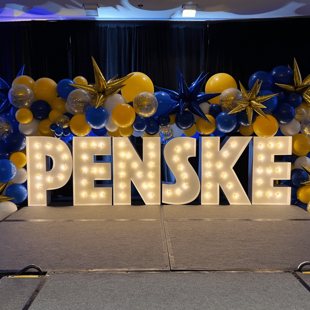 Marquee letters spelling out "PENSKE" surrounded by blue and gold balloons