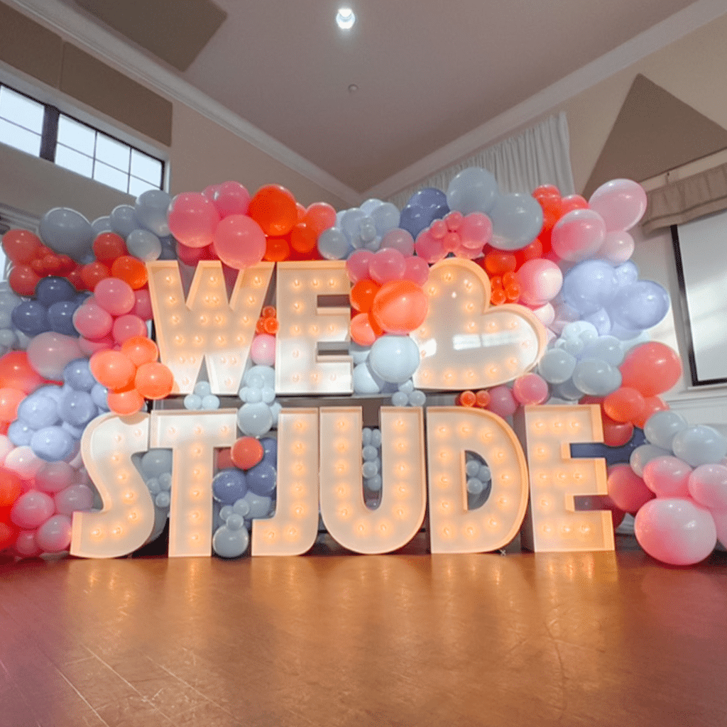 Marquee letters spelling out "WE HEART ST JUDE" surrounded by pink and blue balloons