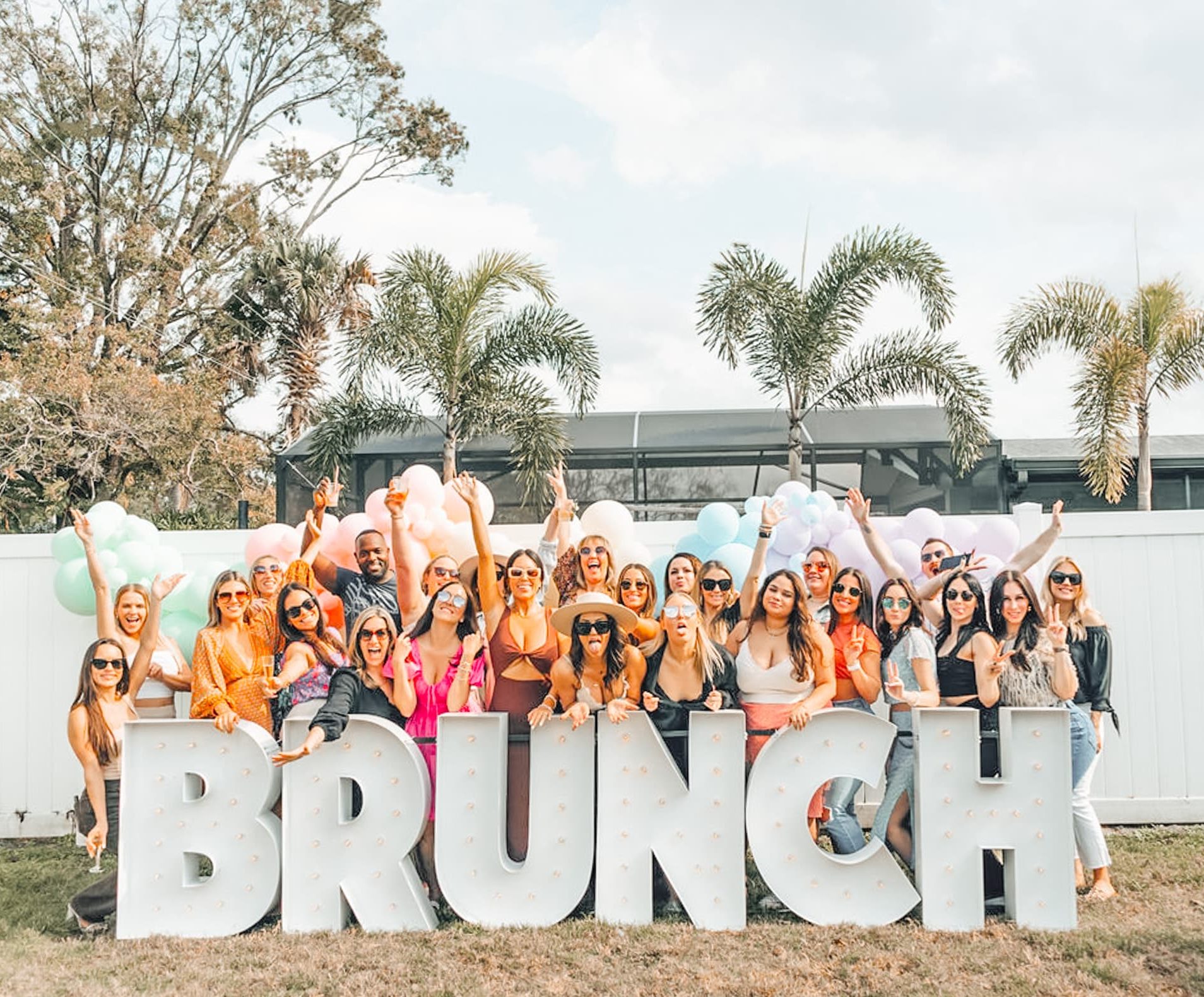 Group of people standing behind light up marquee letters that read BRUNCH