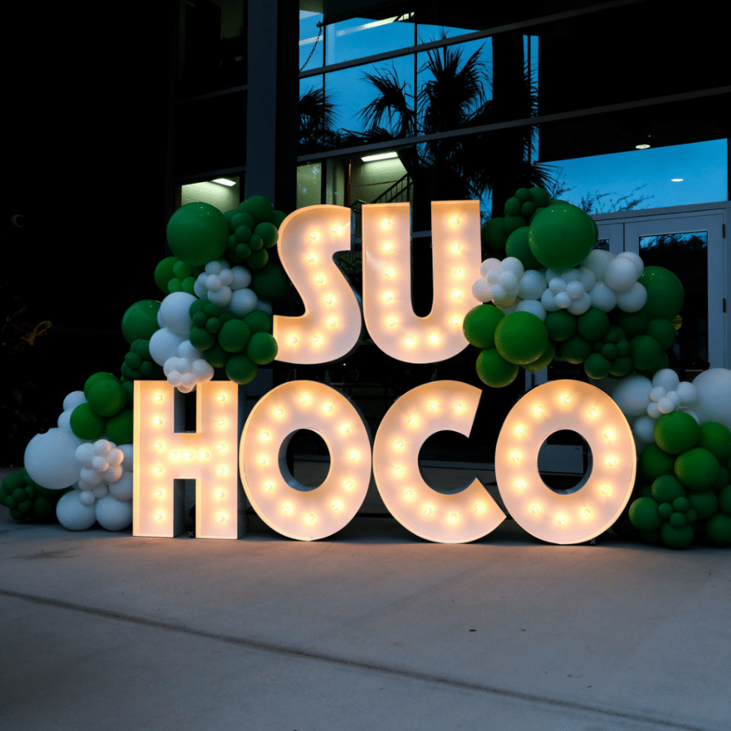 SU HOCO spelled out in marquee lights. There are also green and white balloons