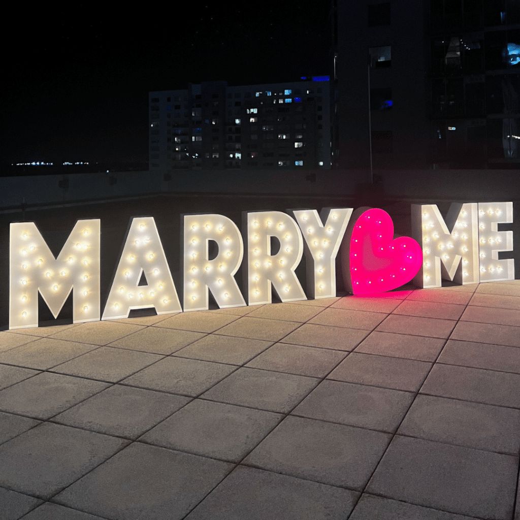 Marriage proposal with marquee letters that spell out "MARRY ME" with a pink heart between the words